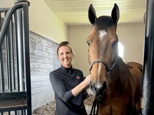 A woman standing next to a horse in a stable.