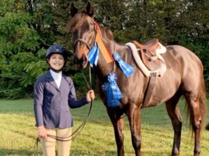 A girl in blue jacket holding reins of horse.